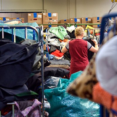 A woman sorting through piles of clothes at a charity shop